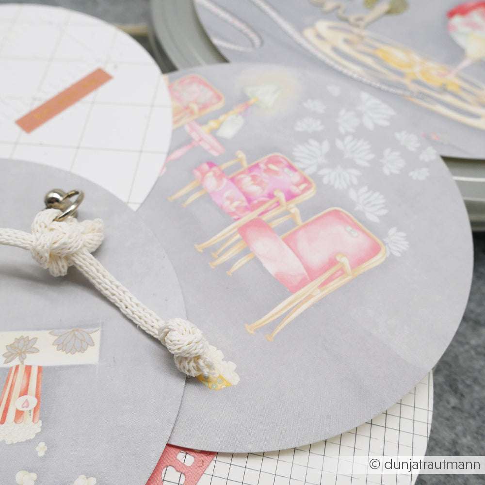 Runde Karten von Alexandra Renke aus Designpapier mit pastellfarbenen Stuhlillustrationen, gehalten von einem weißen Seil auf einer grauen Oberfläche - ideal für Papierprojekte oder Fans von Lisas Figurinen Filmzauber.