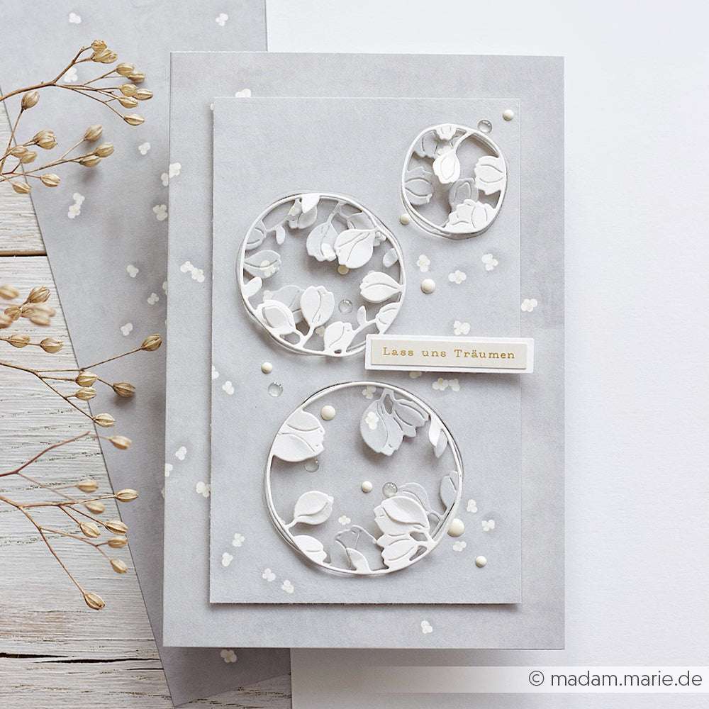Handgefertigte graue Grußkarte von Alexandra Renke mit drei weißen floralen Kreisausschnitten, Perlenakzenten und dem deutschen Label "Lass uns Träumen" - ideal für Papierprojekte oder zur Aufwertung Ihrer eleganten Designpapierkollektion.