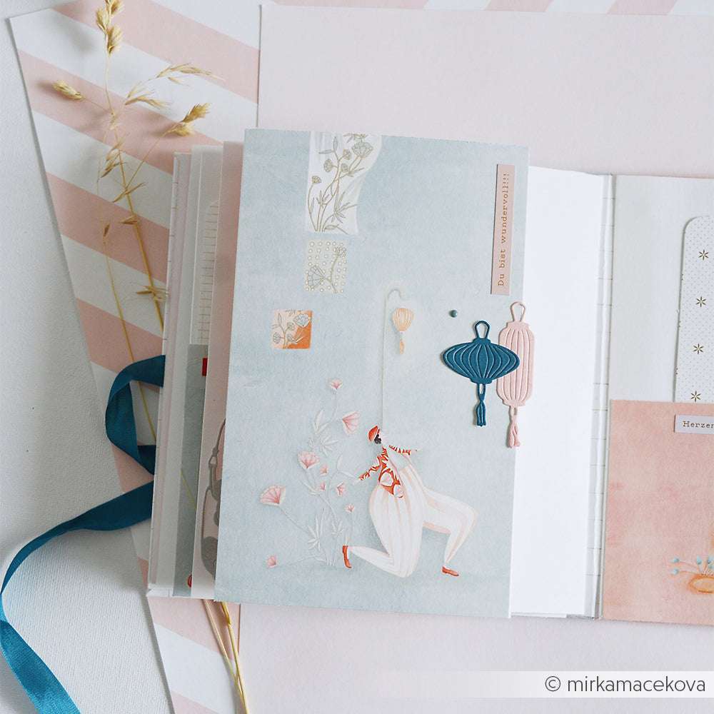 Dekoratives Alexandra Renke Journal mit pastellfarbenem Einband, blauem Band und Blumen- und Laternenmotiven auf weichem Hintergrund - ideal für Ihre Papierprojekte oder kreativen Buchbinderei-Ideen.