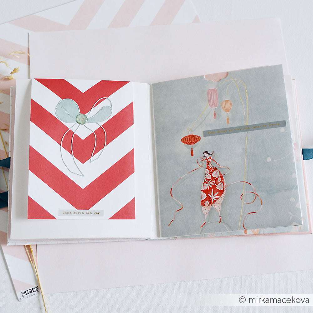 Aufgeschlagenes Buch mit einem Chevron-Herzmotiv auf der linken Seite und einer tanzenden Frau mit Laternen auf der rechten Seite - gefertigt aus Alexandra Renke Designpapier, perfekt für Grußkarten oder Papierprojekte.
