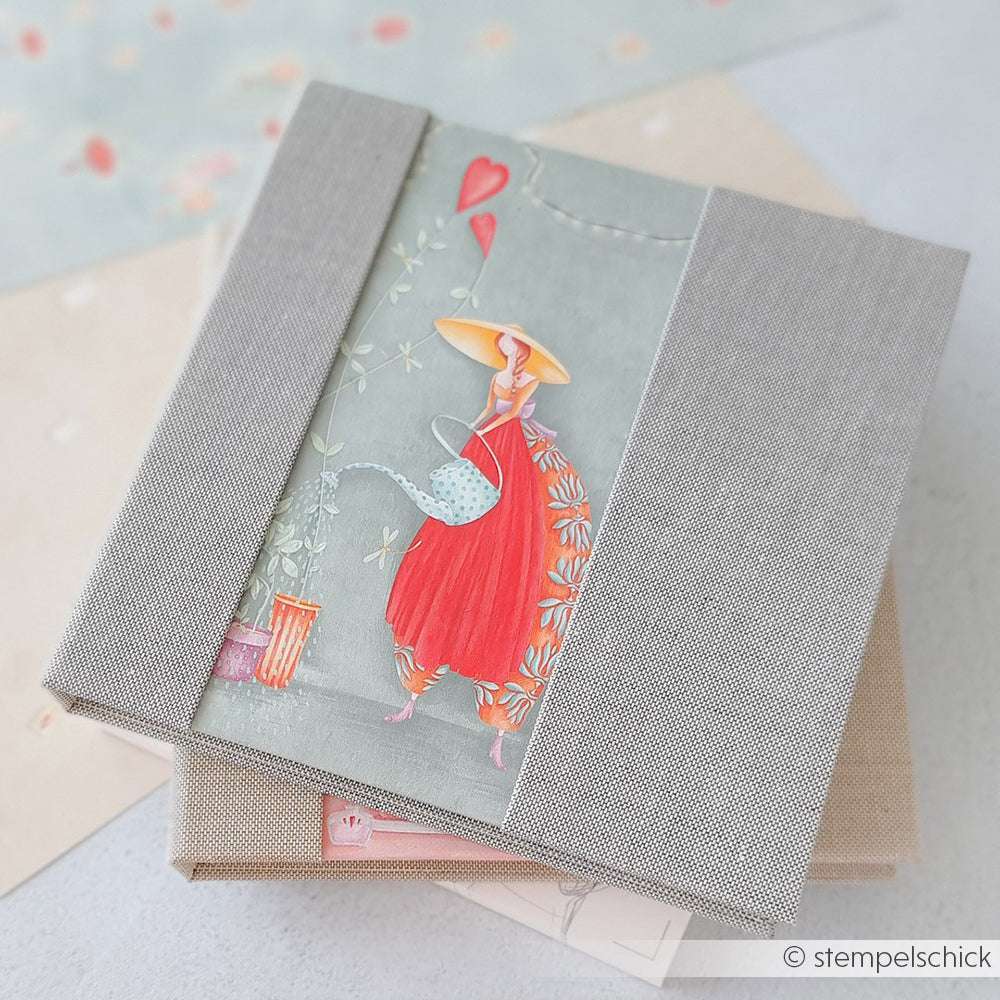 Quadratisches, graues Fotoalbum von Alexandra Renke mit dem Titelbild einer Frau im roten Kleid, die einen Drachen steigen lässt - ideal für Papierprojekte-Fans und alle, die feine Designpapier- und Buchbinderei-Handwerkskunst schätzen.