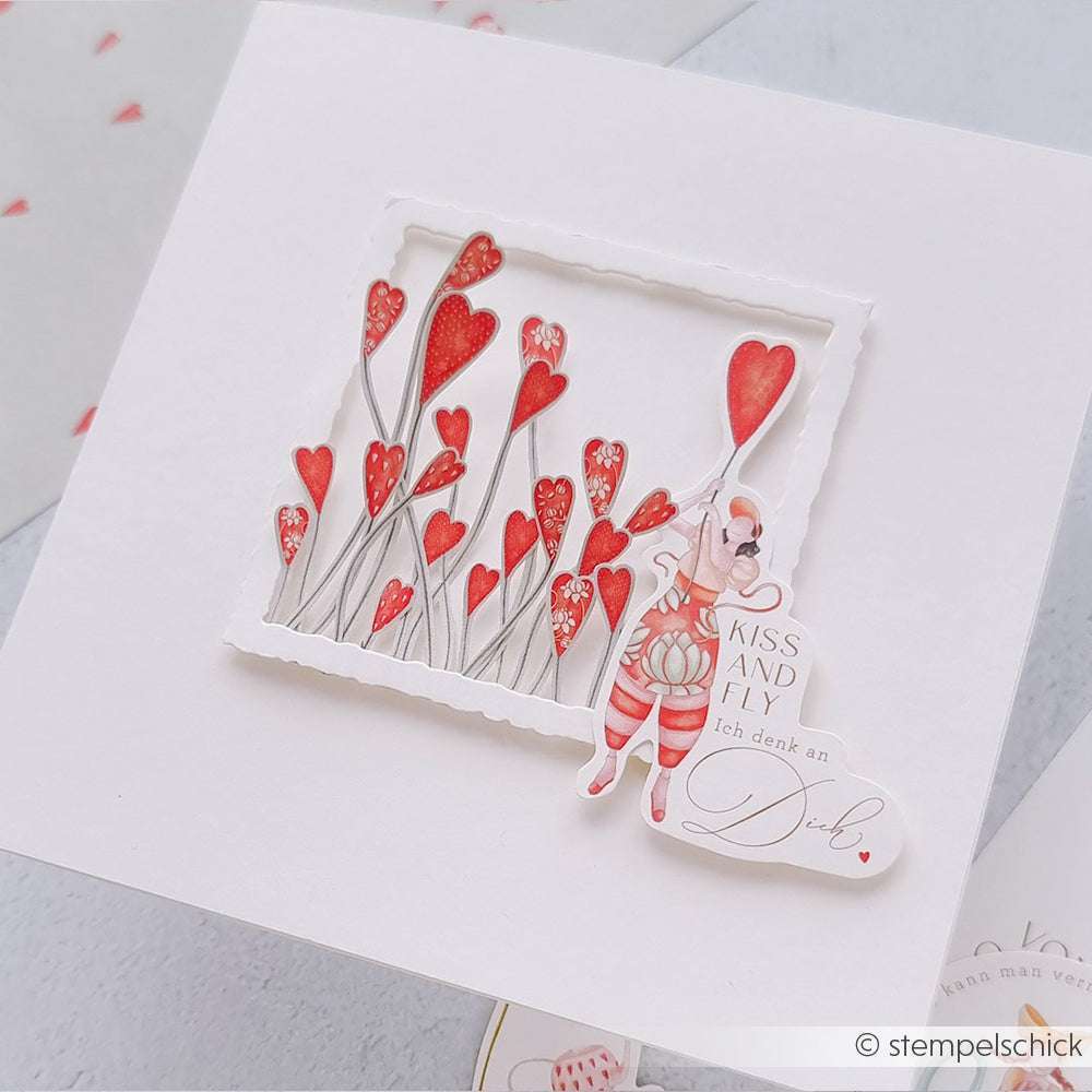Handgefertigte Grußkarten von Alexandra Renke mit roten Herzblumen und einer Figur mit einem herzförmigen Luftballon unter einem Kiss and Fly-Schild - ideal für Ihre Papierprojekte!.