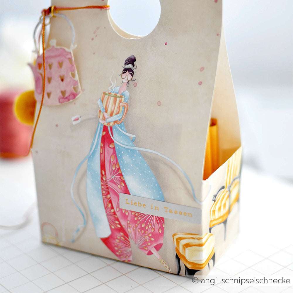 Geschenktüte von Alexandra Renke mit einer illustrierten Frau in einem bunten Kleid, die Teetassen hält. Ideal für Papierprojekte oder Buchbinderei. Text auf Tasche: "Liebe in Tassen.