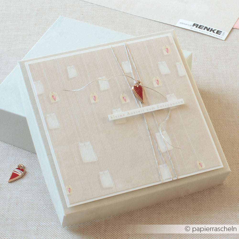 Quadratische Geschenkbox mit weichem beigen Deckel, rotem Herzanhänger und zarter Kordel - ideal für Papierprojekte oder als schöner Akzent für Buchbinderei-Stücke von Alexandra Renke.
