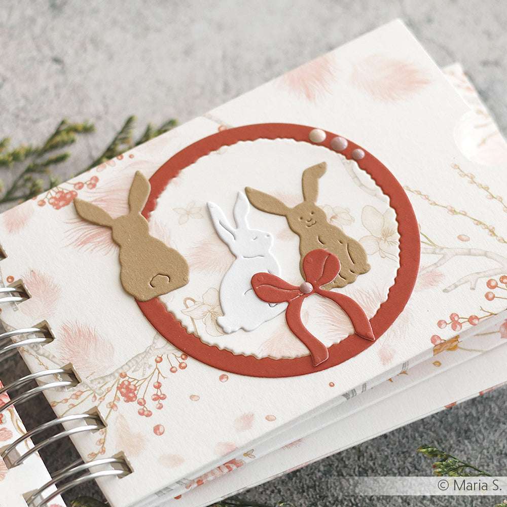 Handgefertigte Alexandra Renke Karte mit drei Hasenausschnitten in einem roten Kreis, verziert mit Schleife und Perlen auf floralem Hintergrund - ideal für Papierprojekte oder als charmantes Buchbinderei-Geschenk.