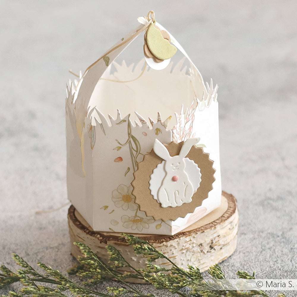 Dekorative Papierschachtel von Alexandra Renke mit Hasenmotiv, floralen Akzenten und Herzanhänger - gefertigt aus hochwertigem Designpapier. Ideal für Papierprojekte oder als charmantes Display neben Grußkarten auf einem Holzsockel.