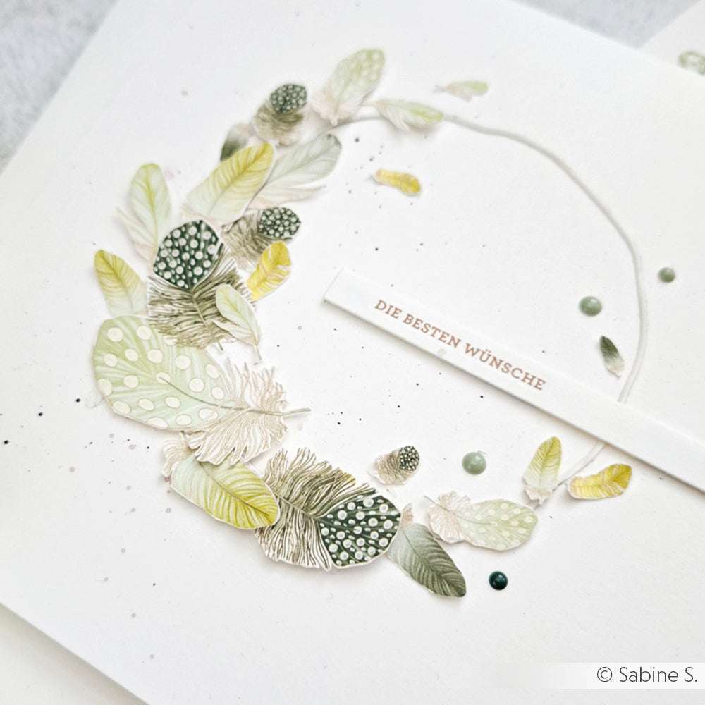 Handgefertigte Karte von Alexandra Renke mit zarten hellgrünen und gelben Federn, feinem Designpapier und "DIE BESTEN WÜNSCHE" auf einem weißen Streifen - ideal für Ihre Papierprojekte.