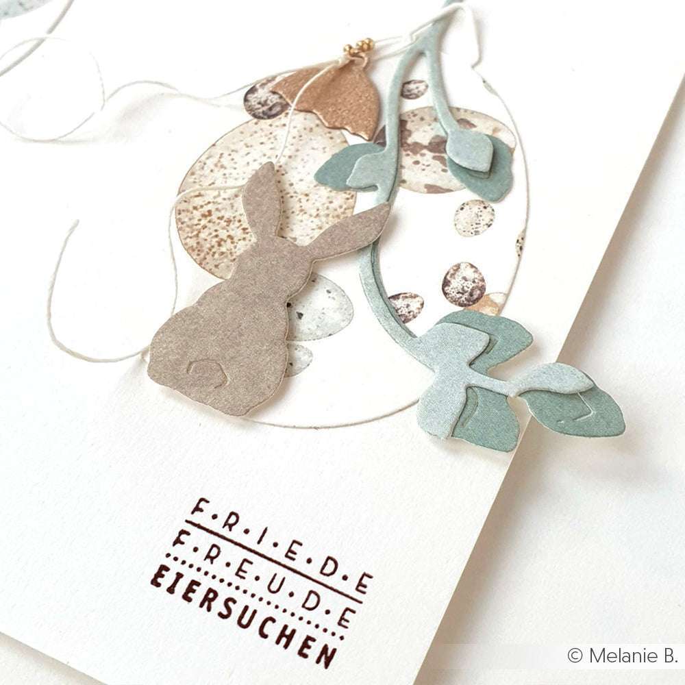 Handgemachte Osterkarte von Alexandra Renke, gestaltet mit Designpapier. Mit Hasensilhouette, Blättern und dem gestempelten Schriftzug "FRIEDE FREUDE EIERSUCHEN" - ideal für Papierprojekte oder Buchbinderei-Fans.
