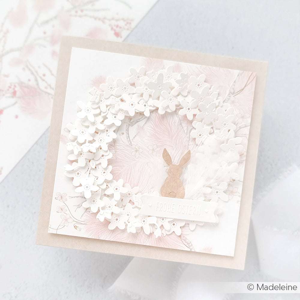 Quadratische Osterkarte von Alexandra Renke mit weißem Blumenkranz, Hasensilhouette und "Frohe Ostern" auf pastellfarbenem Hintergrund - ideal für Papierprojekte oder zur Kombination mit Ihrem Lieblingsdesignpapier.