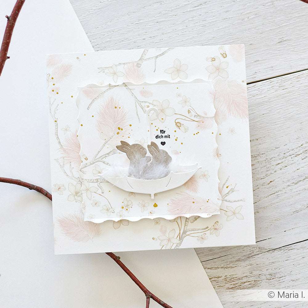 Handgefertigte Grußkarte von Alexandra Renke mit zwei grauen Hasen in einem Papiernest, deutschem Text und goldfarbenem, floralem Designpapier - ideal für Papierprojekte oder als liebevolles Geschenk.