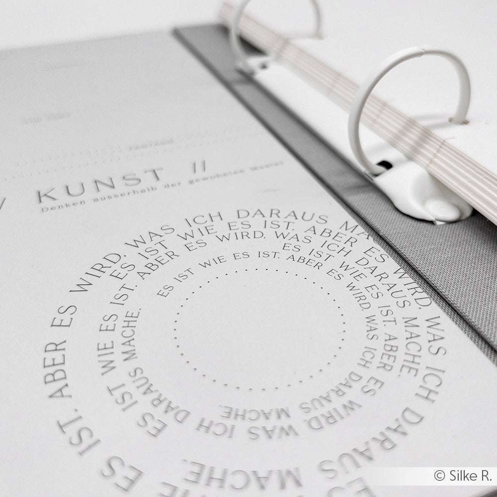 Eine Nahaufnahme einer Alexandra Renke Buchbinderseite mit kreisförmigem deutschen Text und minimalistischem Design, perfekt für Buchbinderei oder kreative Papierprojekte.