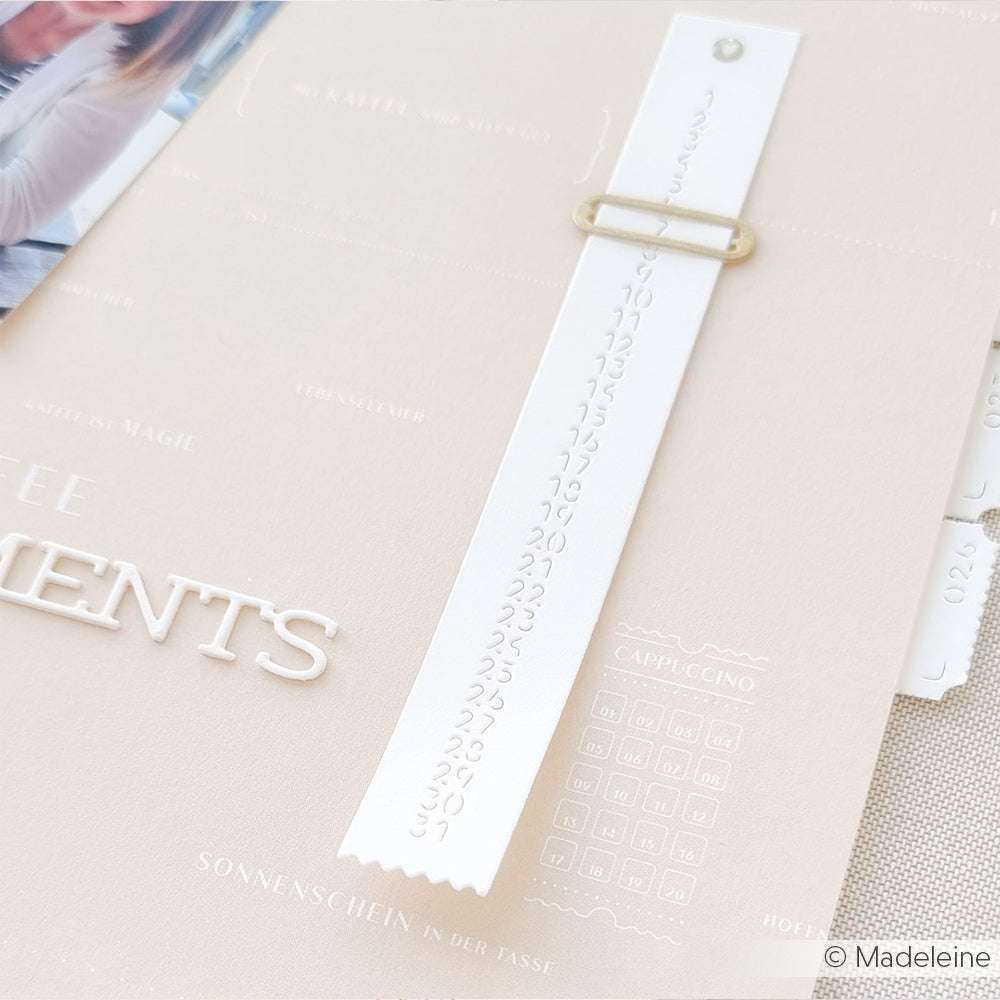 Nahaufnahme einer beigen Karte mit weißem Papierstreifen und geprägten Zahlen, die mit einem goldenen Verschluss befestigt sind - eine ideale Inspiration für Papierprojekte oder in Kombination mit hochwertigem Designpapier von Alexandra Renke.