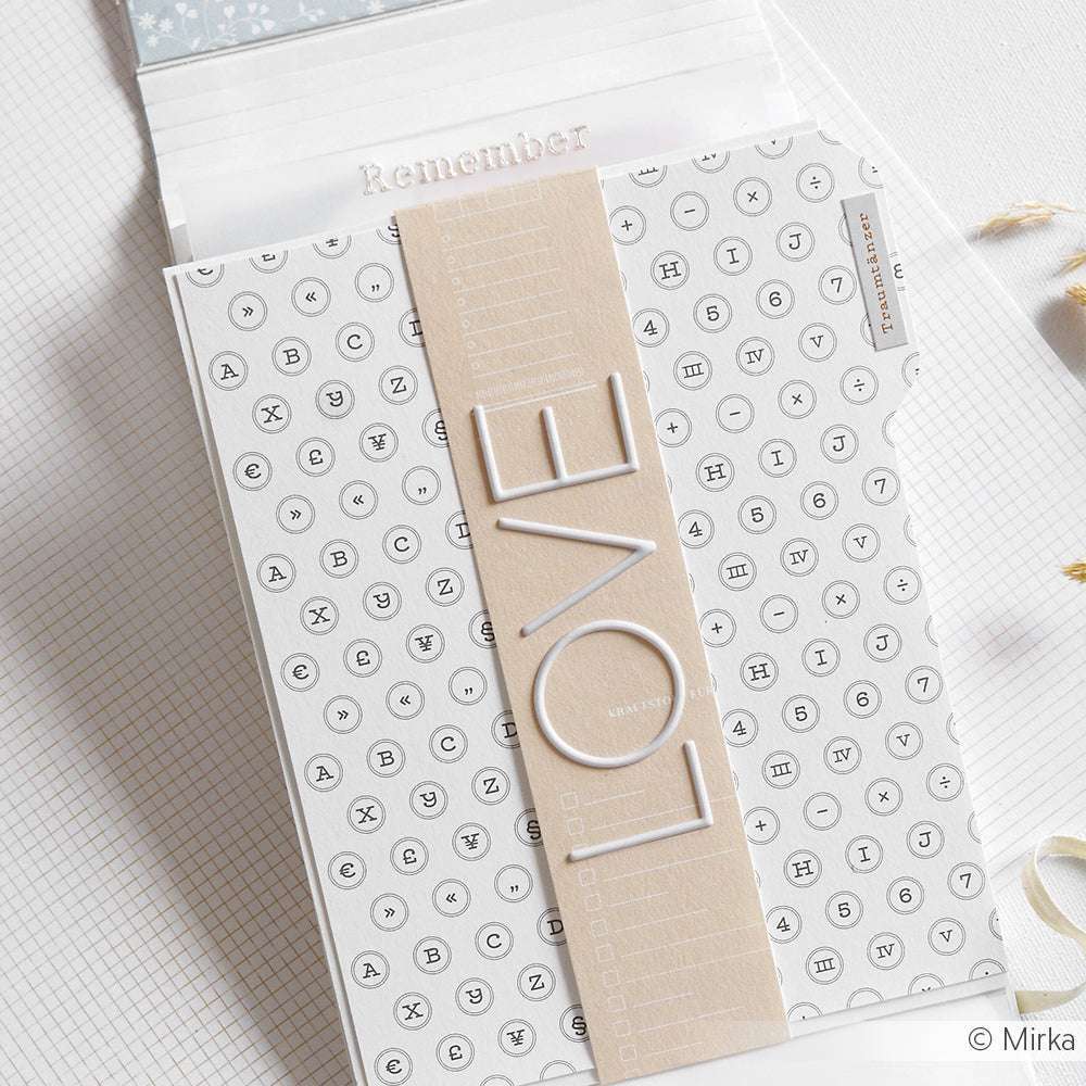 Eine Karte von Alexandra Renke zeigt Buchstaben in Kreisen und ein beigefarbenes Band mit "LOVE" auf stilvollem Designpapier, das auf einer gitterartigen Oberfläche angebracht ist.