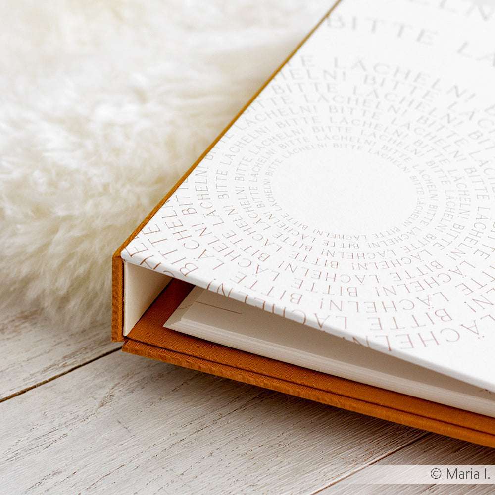 Aufgeschlagenes Buch von Alexandra Renke mit weißem Einband und kreisförmigem Textmuster, hergestellt in Buchbinderei-Technik, ausgestellt auf einer hellen Holzfläche neben einem flauschigen weißen Teppich.