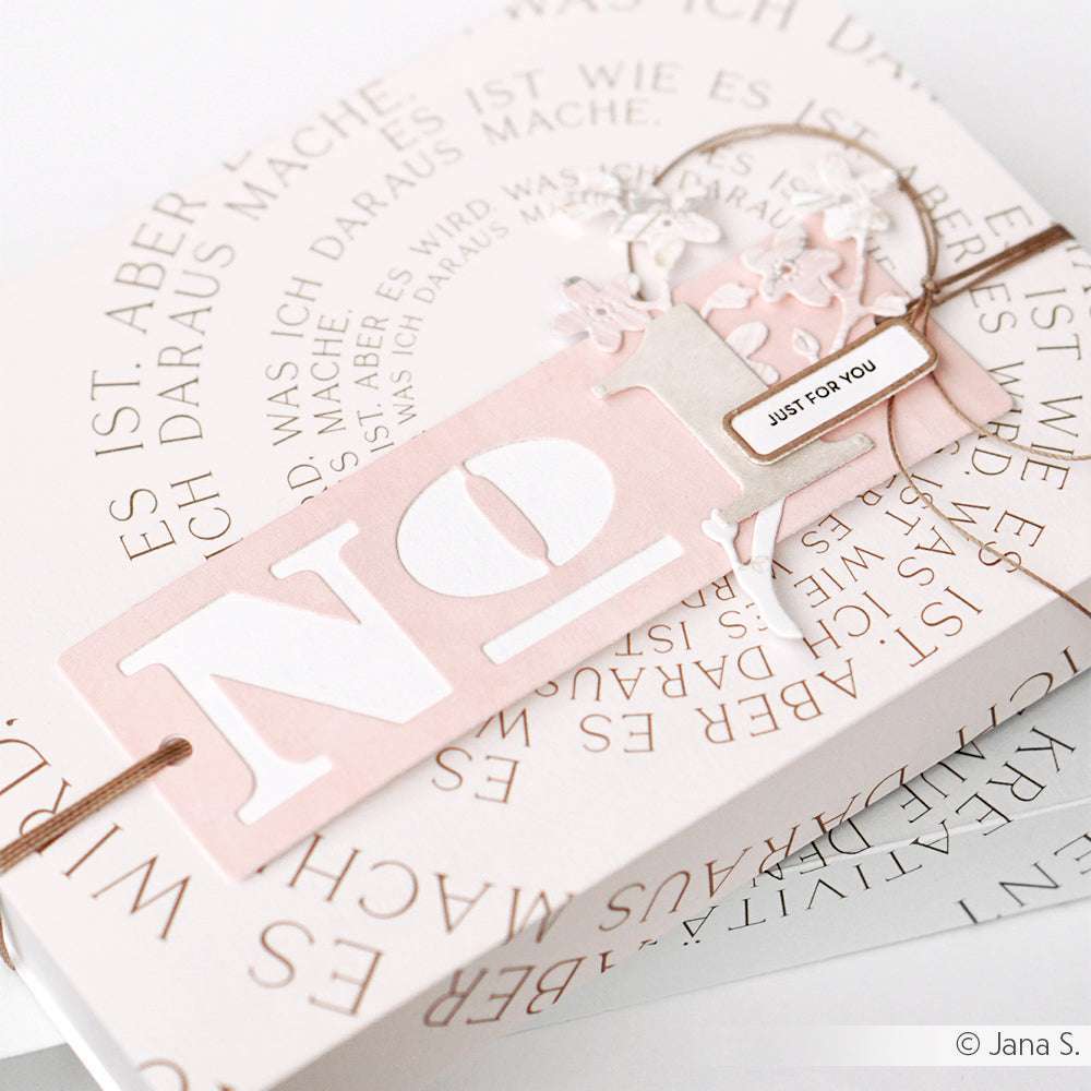 Ein rosafarbener Anhänger mit der Nr. 1 und Just for you auf einer Geschenkschachtel, umrahmt von einem kreisförmigen deutschen Text - perfekt für Alexandra Renke Papierprojekte oder zur Aufwertung Ihrer Buchbinderei-Kreationen.