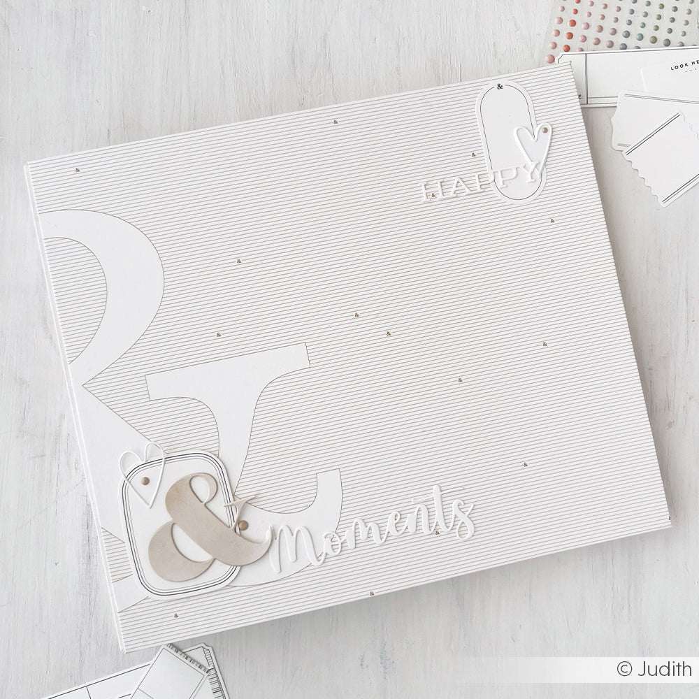 Ein minimalistisches Scrapbook-Cover von Alexandra Renke mit dem Motiv "Glückliche Momente" und einem kaufmännischen Und-Zeichen auf gestreiftem Designpapier - ideal für Ihre nächste Papierprojekte oder Buchbinderei-Kreation.
