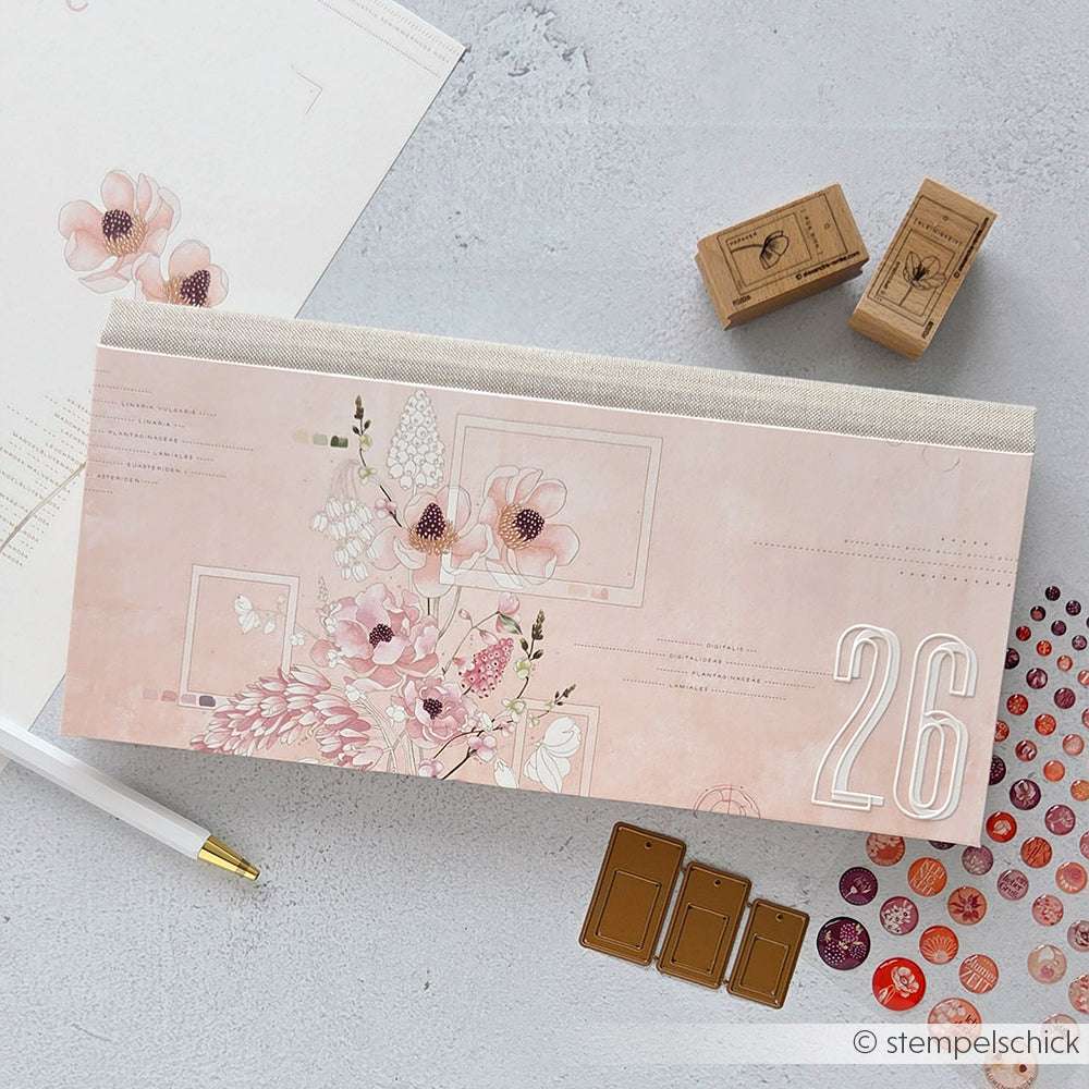 Ein geblümter Tischkalender von Alexandra Renke, Stempel, Stift, Designpapier und dekorative Aufkleber sind kunstvoll auf einer hellgrauen Oberfläche angeordnet.
