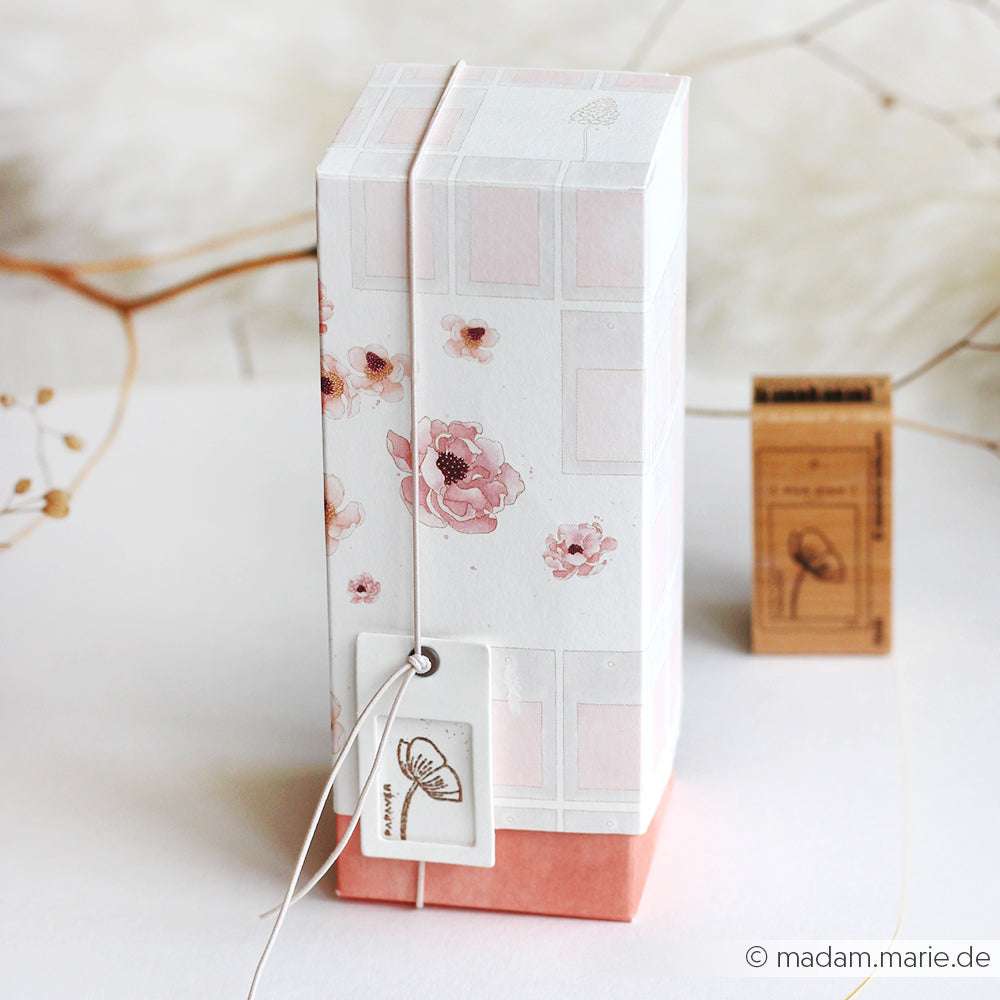 Hohe, rechteckige, florale Geschenkbox von Alexandra Renke mit einem Anhänger, verziert mit zartrosa und weißem Designpapier, inspiriert von kreativer Blütenpracht, ausgestellt auf einer weißen Fläche.