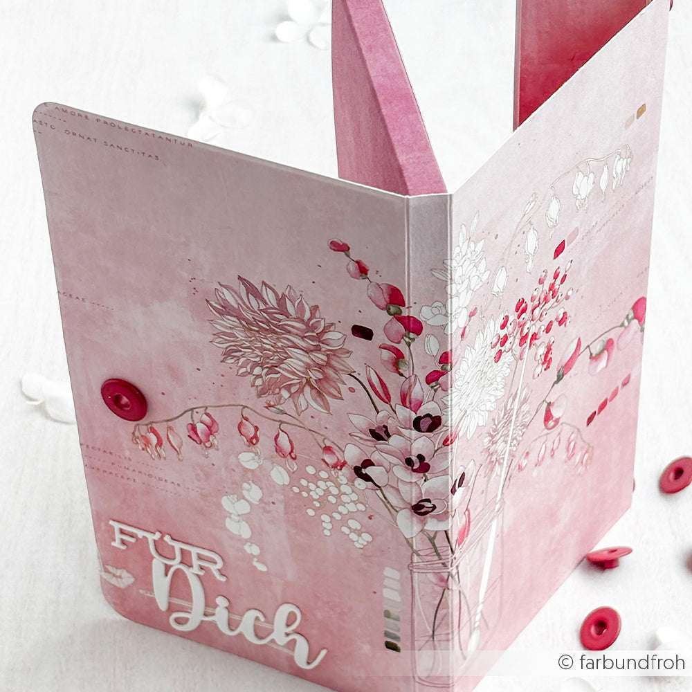 Die rosafarbene Blumengrußkarte von Alexandra Renke aus Designpapier mit dem Text "Für Dich" ist offen auf einer weißen Fläche mit roten Knöpfen - ideal für Papierprojekte oder mit einem hübschen Dahlienstrauß-Motiv.