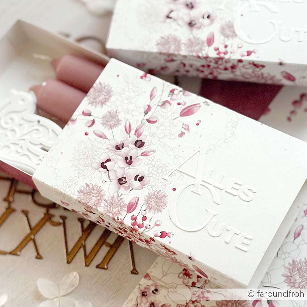 Weiße florale Geschenkbox von Alexandra Renke mit ALLES GUTE-Prägung, rosa Kerzen und Dekoartikeln - ideal für Papierprojekte oder zum Verschenken, unterstrichen von eleganten Designpapier-Akzenten.