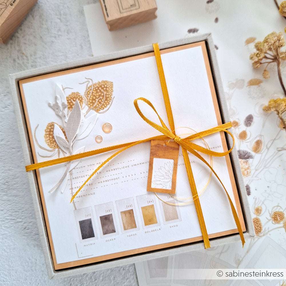 Elegante Geschenkbox von Alexandra Renke mit gelbem Band, getrockneten Blumen und einer Karte mit Farbpalette - ideal für Papierprojekte oder als Inspiration für Ihre nächste Designpapierkreation.