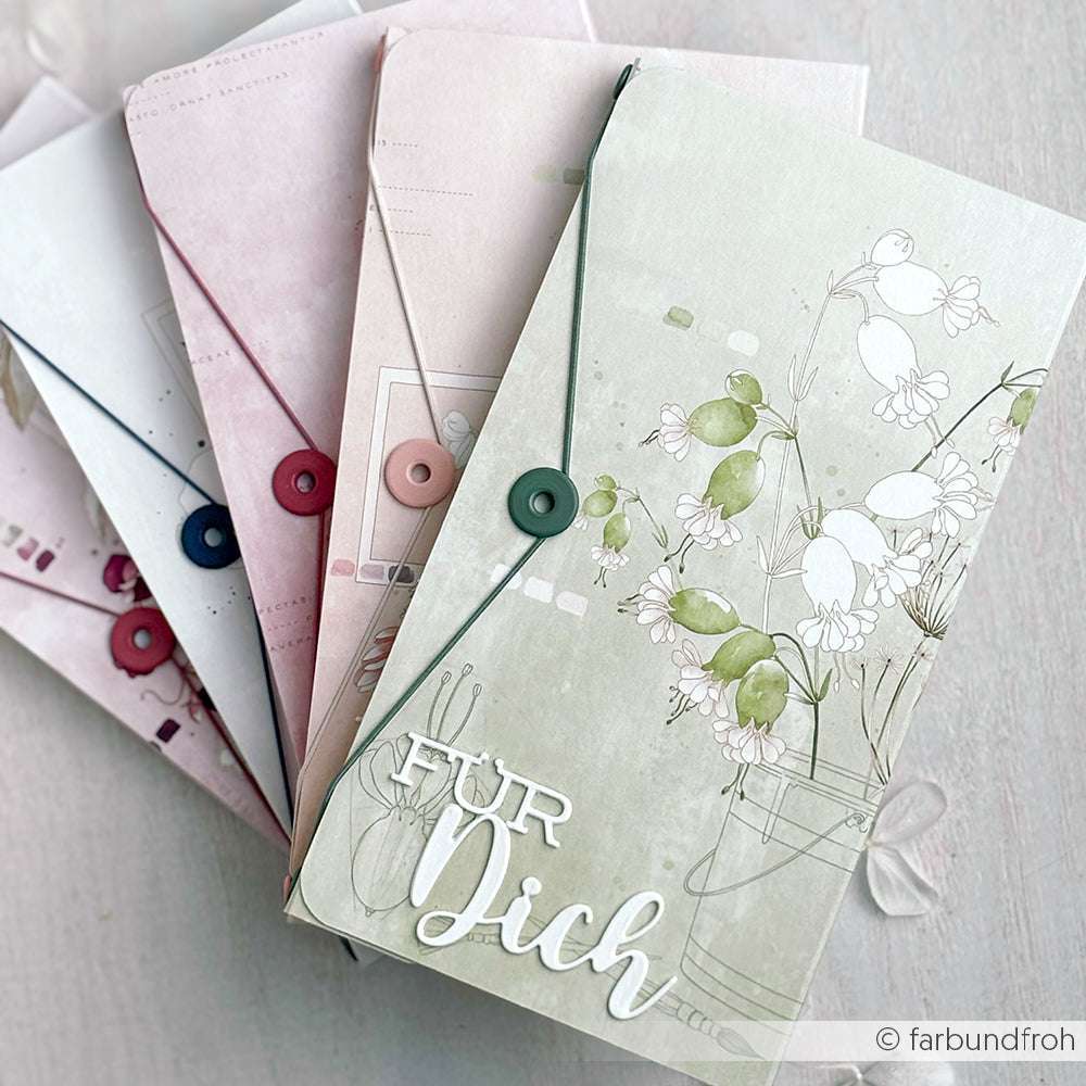 Vier pastellfarbene Briefumschläge von Alexandra Renke mit Knopf- und Kordelverschluss, darunter einer mit "Für Dich" und floralem Design - ideal für kreative Papierprojekte oder zum Verschenken eines handgemachten Gräserstraußes.
