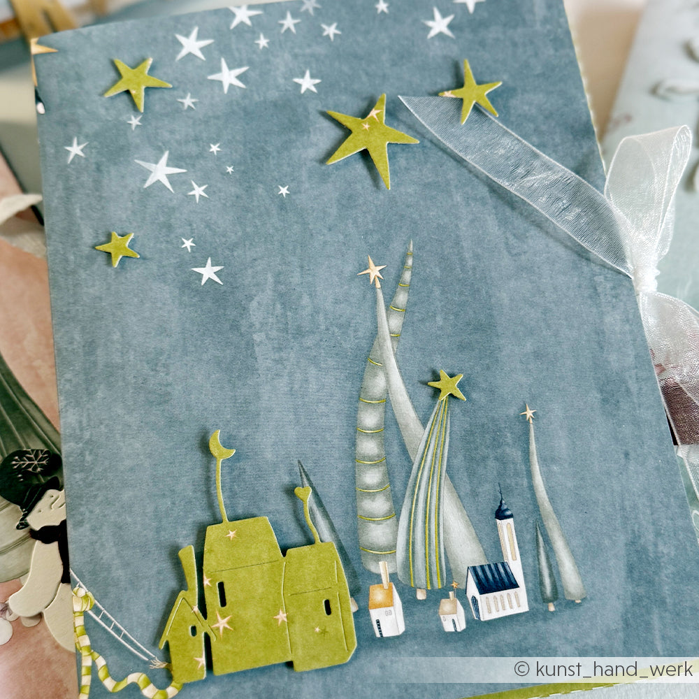Handgefertigte Grußkarten von Alexandra Renke mit skurrilen Gebäuden und Sternen auf blauem Hintergrund, gebunden mit einer weißen Schleife - ideal für Papierprojekte und Weihnachtsgeschenke.