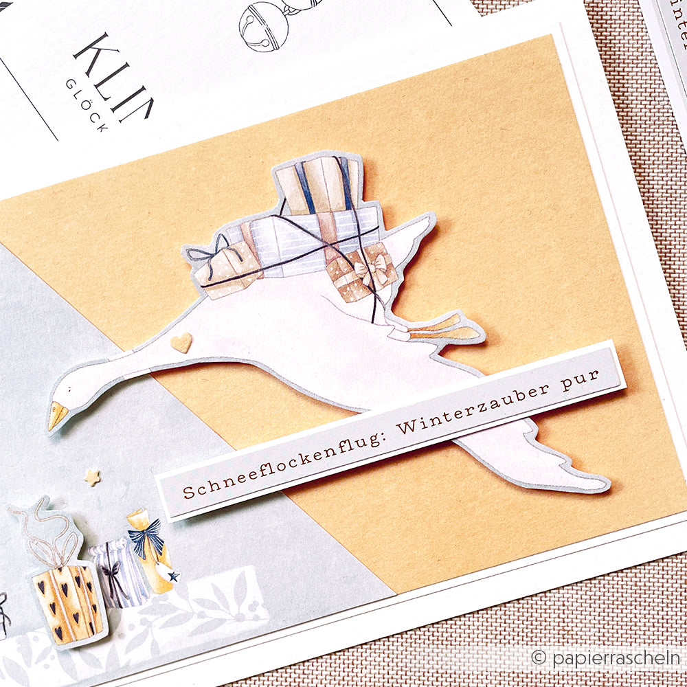 Illustration einer fliegenden Gans, die Geschenke trägt, mit deutschem Text "Schneeflockenflug: Winterzauber pur"-ideal für festliche Papierprojekte und Designpapier Weihnachten von Alexandra Renke.