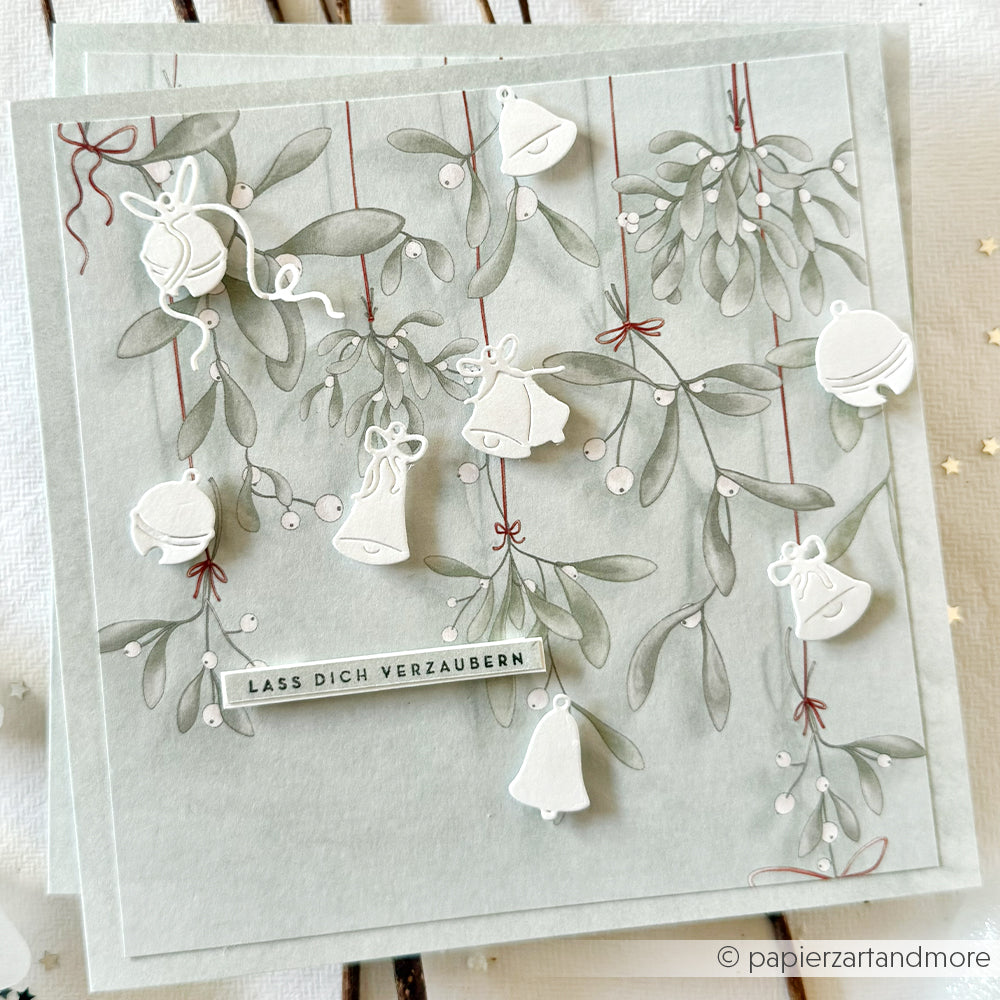 Ein festliches Grußkarten-Design von Alexandra Renke mit weißen Glocken und Mistelzweigen auf hellem Hintergrund mit dem Text "Lass dich verzaubern" - ideal für Papierprojekte oder als Designpapier-Weihnachtsinspiration.