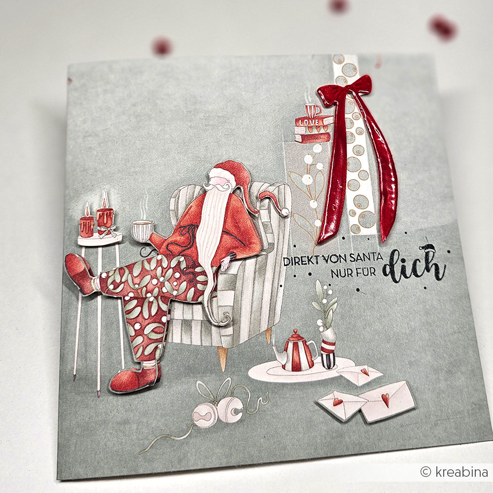 Illustrierter Weihnachtsmann, der sich in einem Sessel mit Geschenken, Tee und Briefen ausruht; mit Alexandra Renke Designpapier Weihnachten Details und deutschem Text auf der Karte.