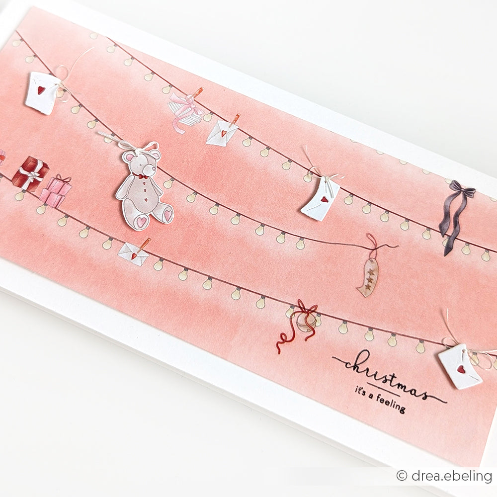 Eine rosafarbene Weihnachtskarte von Alexandra Renke, verziert mit Lichterketten, Mini-Umschlägen, Geschenken, einem Teddybär, Designpapier-Akzenten und Girlandenzauber, mit der Überschrift "Weihnachten ist ein Gefühl".
