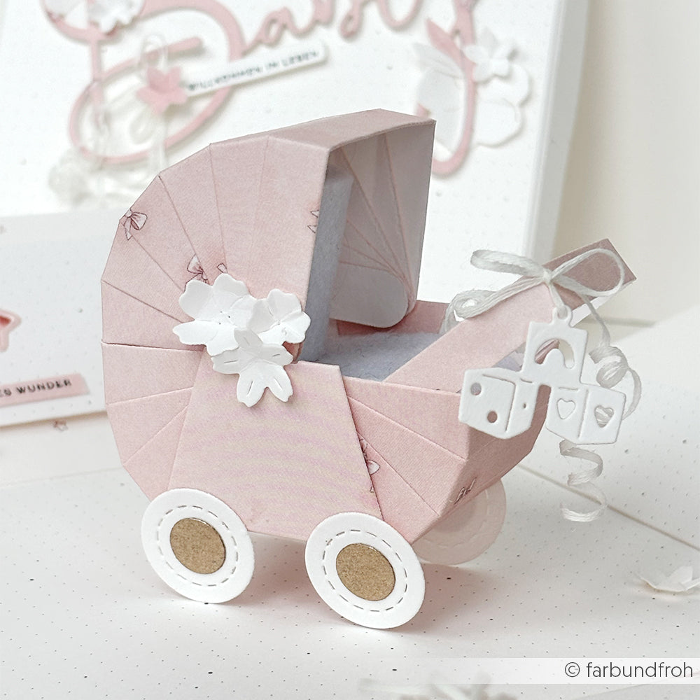 Handgefertigter rosafarbener Kinderwagen von Alexandra Renke aus Designpapier mit weißen Rädern, floralen Akzenten und Mini-Geschenkschachtel-Anhängern - eine bezaubernde Note für Ihre Papierprojekte.