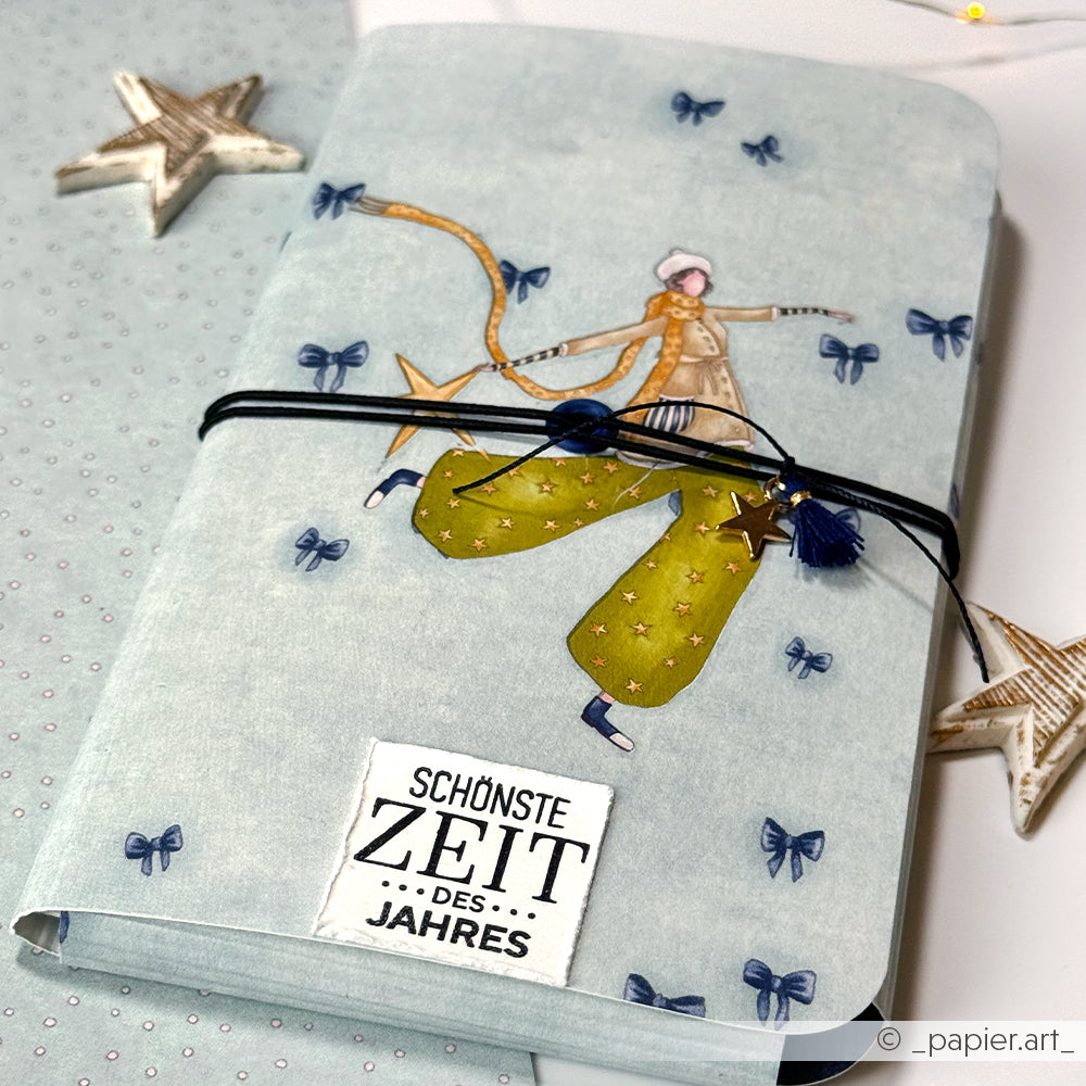 Alexandra Renke Notizbuch mit einer illustrierten Figur in grüner Hose, blauen Schleifen und dem Text SCHÖNSTE ZEIT DES JAHRES - ideal für Papierprojekte oder zum Hervorheben Ihres Lieblingsdesignpapiers.