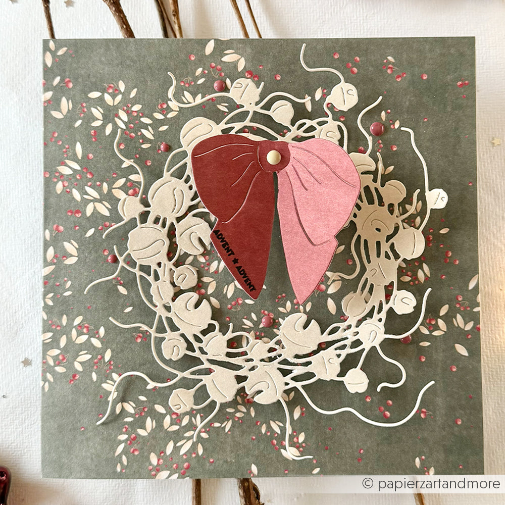 Eine handgemachte Grußkarte von Alexandra Renke mit geschichteten Papierblättern und einem Blumenkranz auf grünem Designpapier - ideal für kreative Papierprojekte.