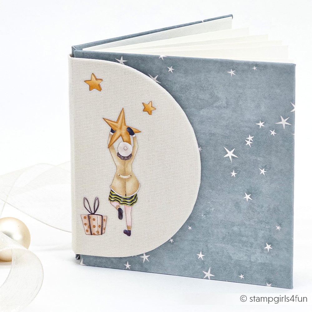 Das blaue Alexandra Renke Sternenzauber Sturmpetrol Notizbuch zeigt ein Mädchen, das nach den Sternen greift, mit einer Geschenkbox - perfekt für Papierprojekte oder kreative Designpapierideen.