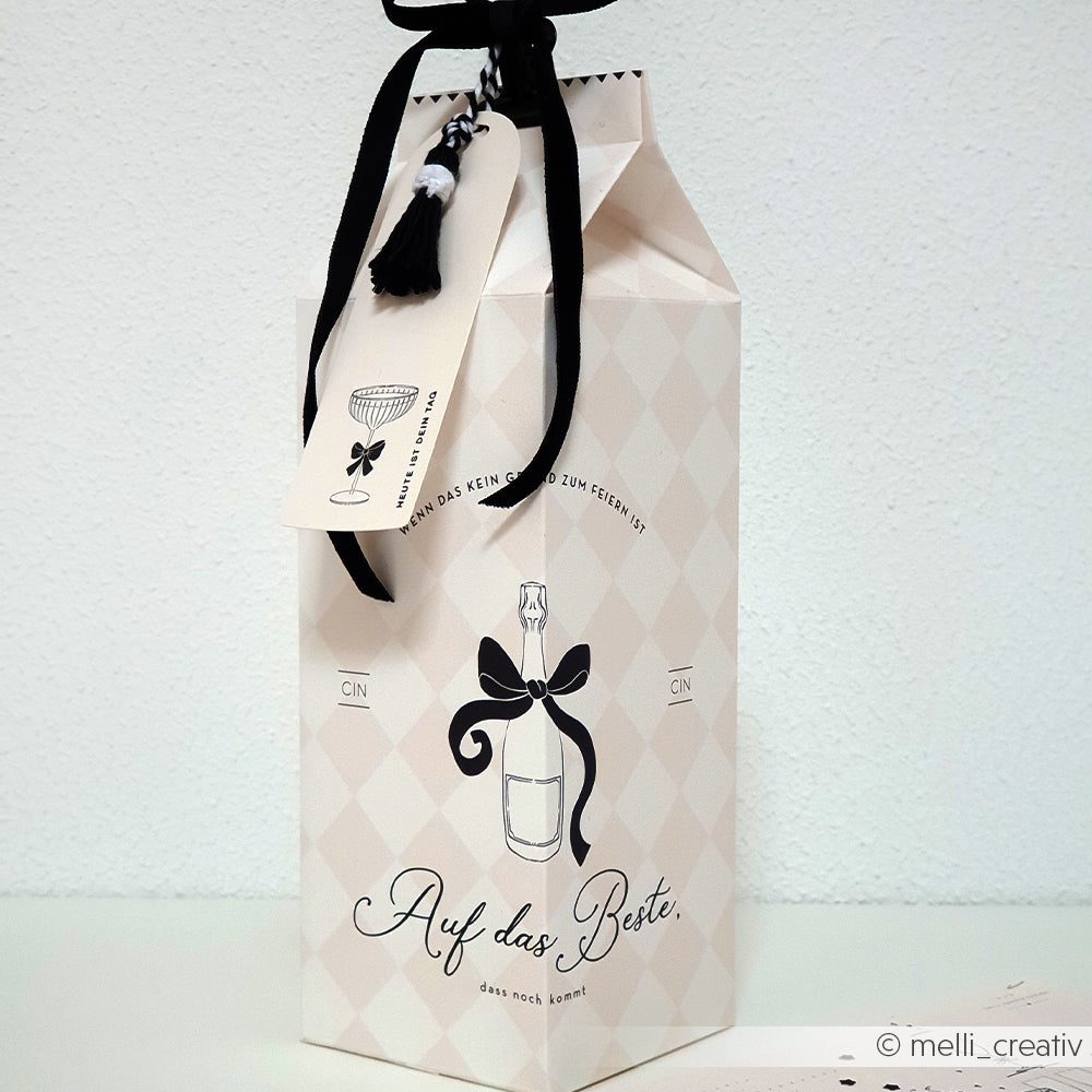 Cremefarbene Alexandra Renke Geschenkbox mit schwarzer Schleife, Weinglasanhänger und dem Text "Auf das Beste!" - ideal für Papierprojekte oder stilvolle Buchbinderei-Geschenke.