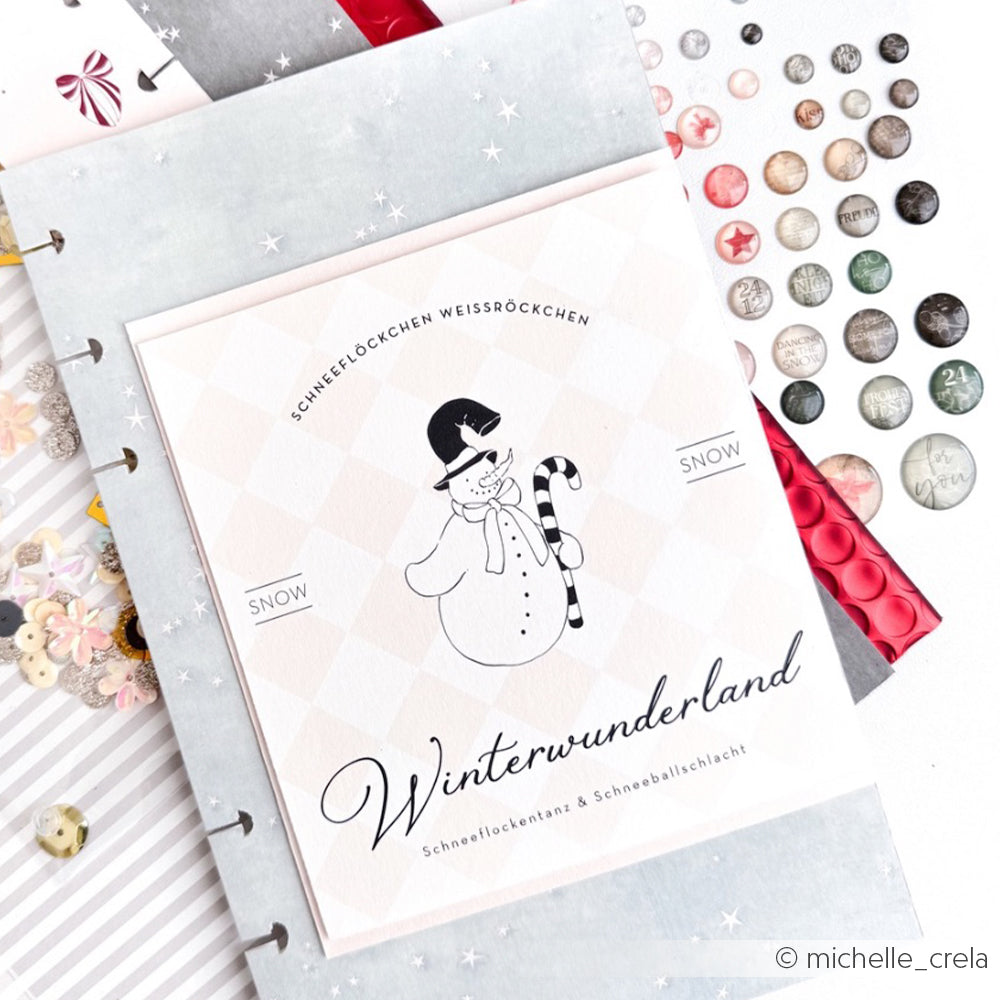 Ein offenes Scrapbook mit der Winterwunderland-Karte von Alexandra Renke, passendem Designpapier und dekorativen Stickern auf weißem Untergrund - perfekt für Papierprojekte und kreative Buchbinderei-Inspiration.