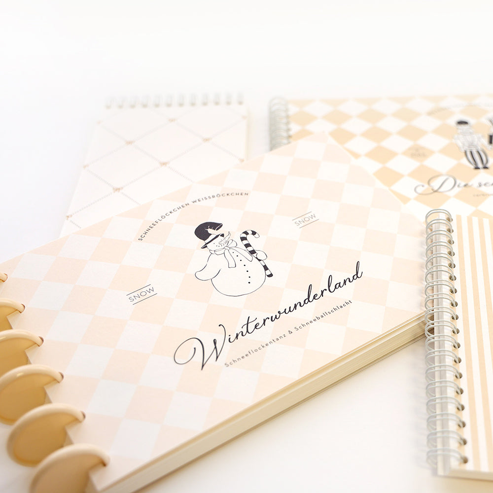 Drei beige-weiße Notizbücher mit Winter- und Schneemannmotiven aus Alexandra Renke Designpapier Winterwunderland, angeordnet auf einer weißen Fläche.