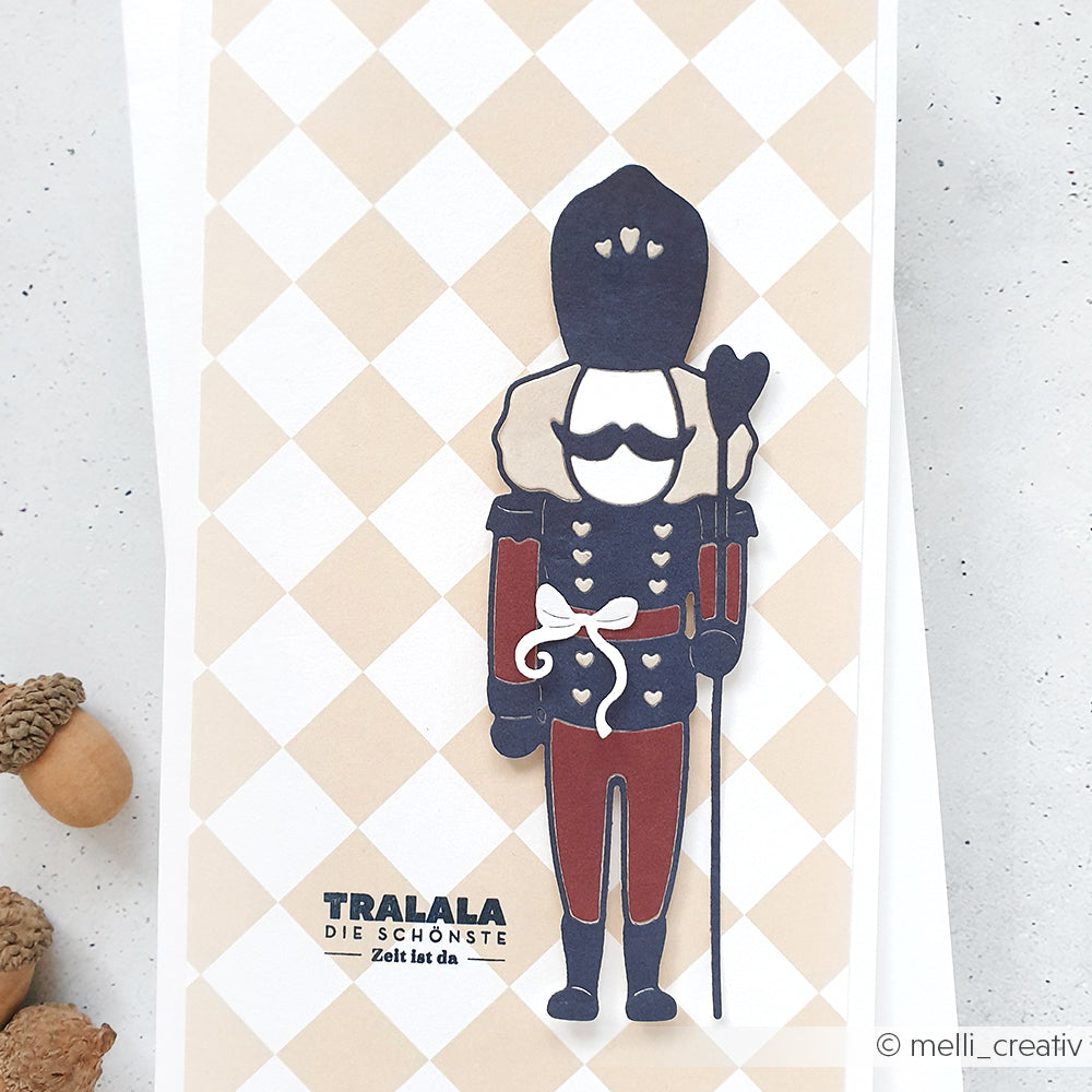 Papierbastel-Nussknacker-Soldat auf Alexandra Renke Großes Karo beige Designpapier, akzentuiert mit deutschem Text und Eicheln-ideale Inspiration für Ihre festlichen Papierprojekte.