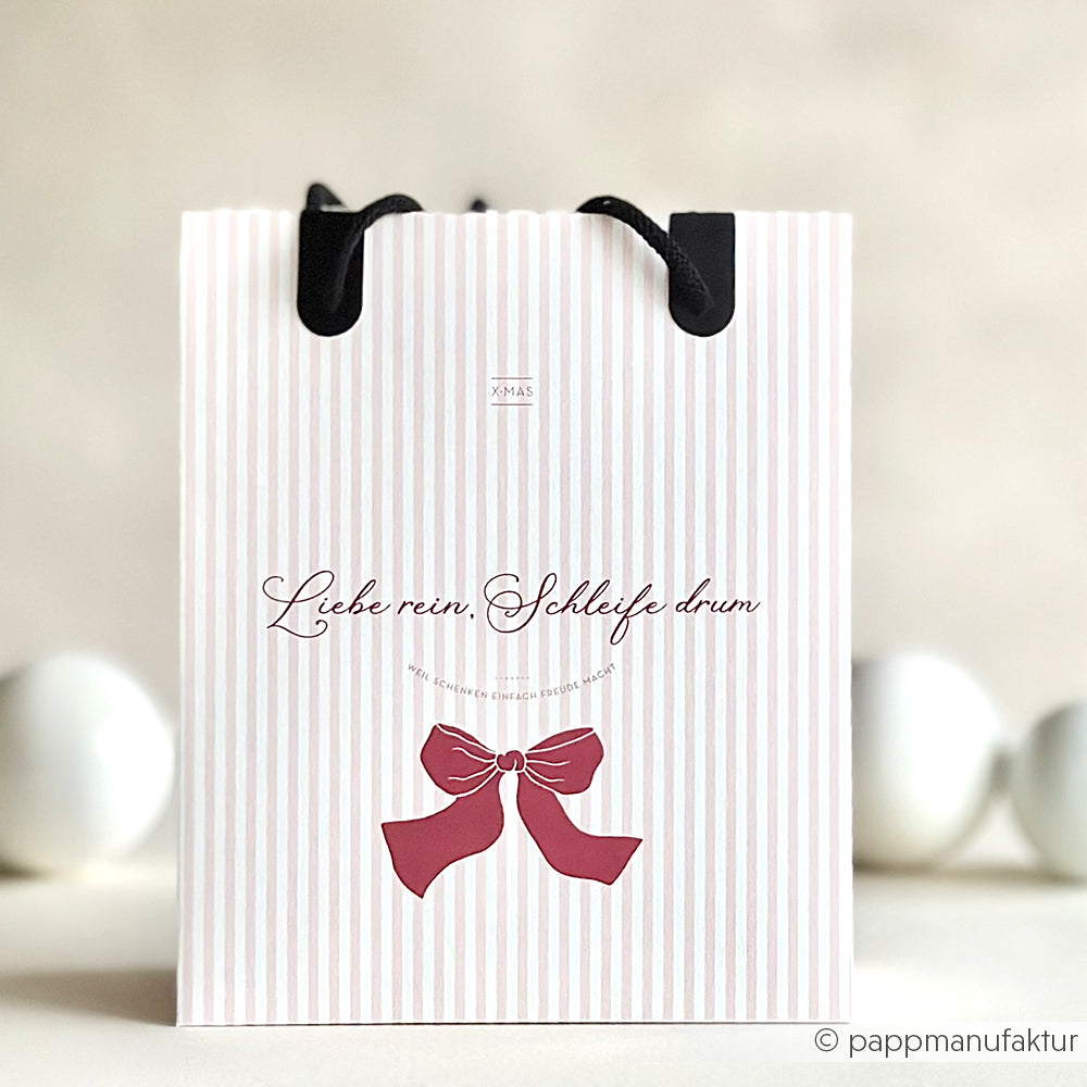 Die gestreifte Geschenktasche von Alexandra Renke aus hochwertigem Designpapier hat schwarze Griffe und eine große rote Schleife auf der Vorderseite.