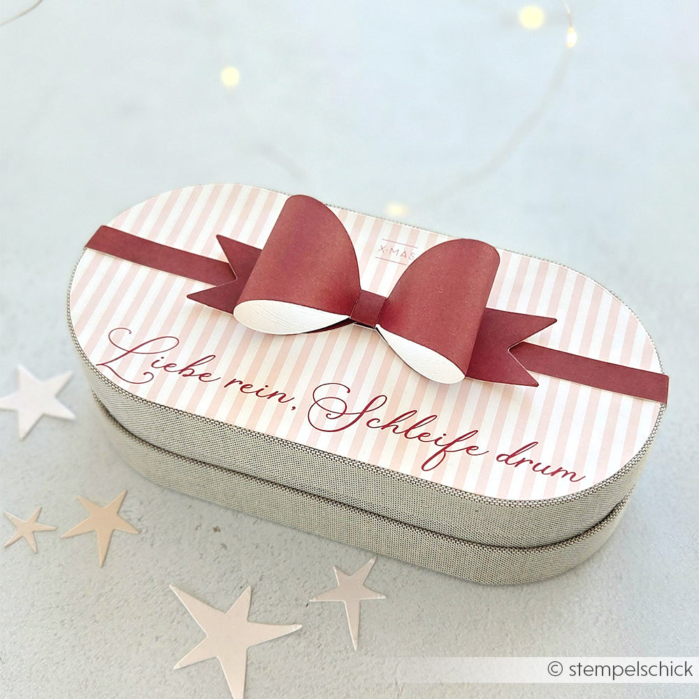 Rechteckige Geschenkbox von Alexandra Renke mit rosa Schleife, gefertigt aus Designpapier. Auf dem Deckel steht der Text "Liebe rein. Schleife drum." Ideal für Papierprojekte oder Kreationen der Buchbinderei.