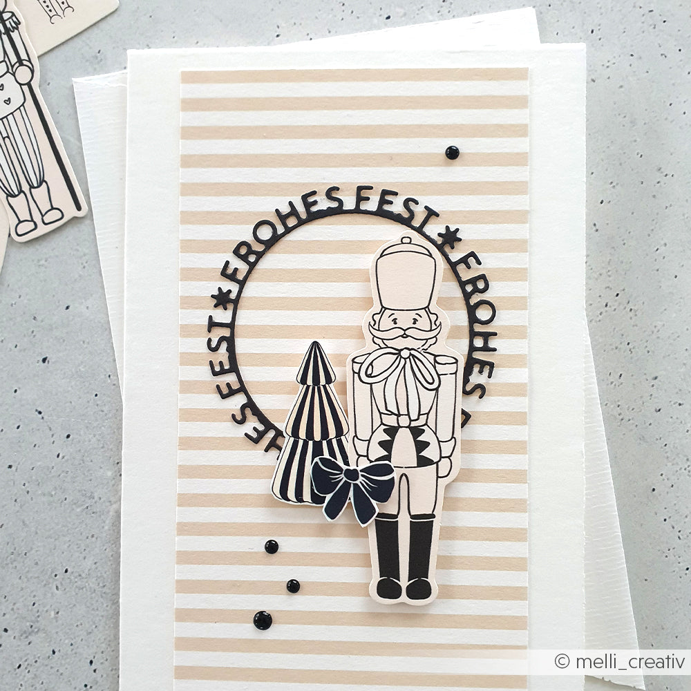 Handgemachte Karte von Alexandra Renke mit Nussknacker, Baum und "Frohes Fest" auf beige und rosa gestreiftem Papier - ein charmantes Highlight für festliche Papierprojekte.