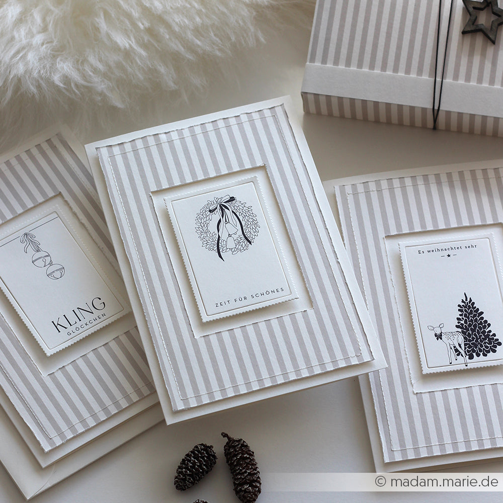 Drei elegante, gestreifte Weihnachtskarten von Alexandra Renke mit exquisitem Designpapier und schlichten schwarz-weißen botanischen Illustrationen liegen anmutig auf einem Tisch.