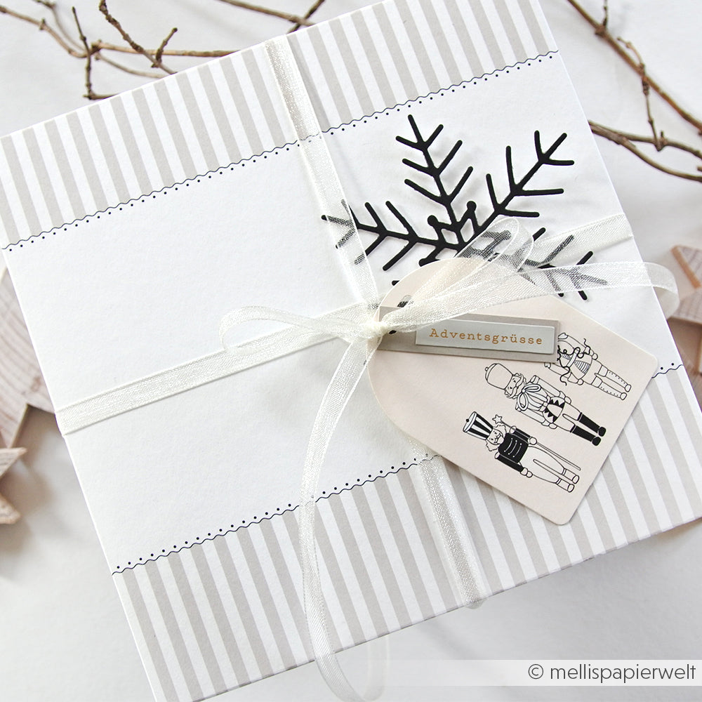 Quadratische weiße Geschenkschachtel mit Schleife, Schneeflocken-Dekor und weihnachtlichen Anhängern mit Nussknacker-Motiven von Alexandra Renke - ideal für Papierprojekte oder um den Kreationen von Buchbinderei und Designpapier ein festliches Flair zu verleihen.