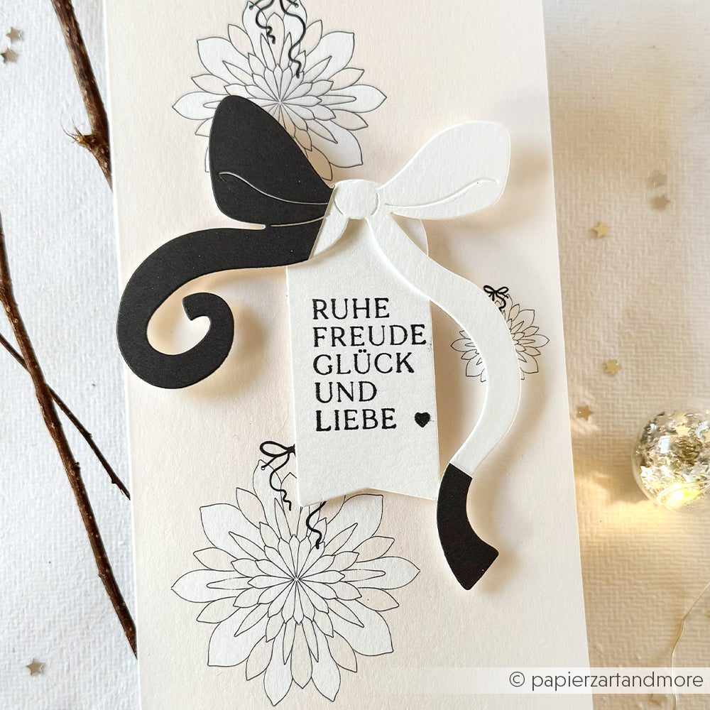 Weiße Karte von Alexandra Renke mit schwarzen Blumenzeichnungen, einer schwarz-weißen Schleife und deutschen Wünschen für Frieden, Freude, Glück und Liebe - ideal für elegante Papierprojekte mit Designpapier.