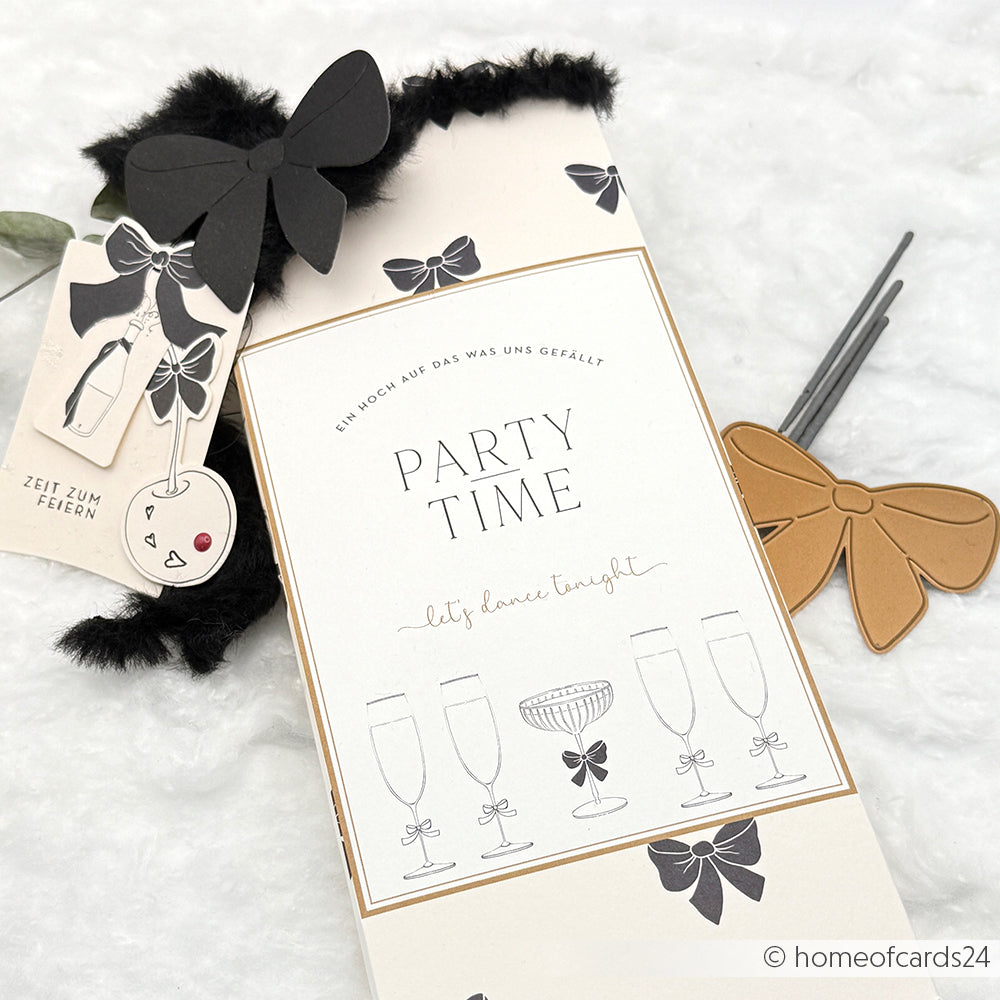 Partyeinladungskarte von Alexandra Renke aus elegantem Designpapier mit schwarzer und goldener Schleife sowie einem festlichen Kirschanhänger.
