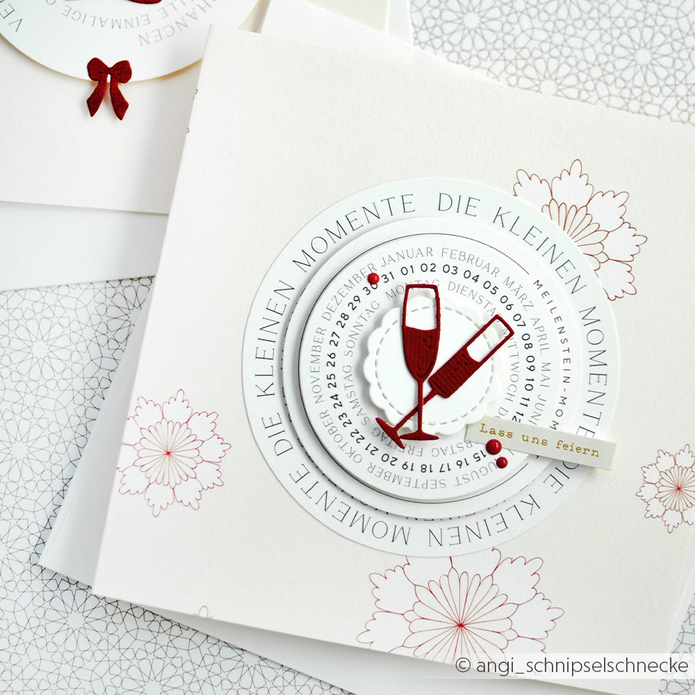 Eine Grußkarte von Alexandra Renke aus Designpapier mit Sektgläsern, Kalendertext und dem Spruch "Die kleinen Momente feiern".