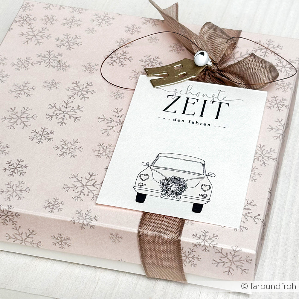 Eine rosa Geschenkbox mit Schneeflockenmuster, braunem Band und einer Karte aus dem Set Liebe im Gepäck von Alexandra Renke - ideal für Papierprojekte und deutsche Urlaubsgrüße.