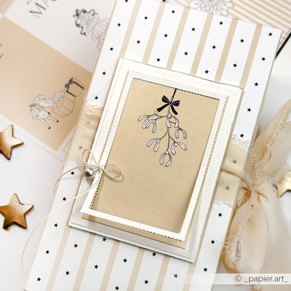 Das Geschenk ist in beigefarbenem Alexandra Renke Designpapier mit Sternen und Streifen verpackt und mit einer Mistelkarte und Perlen verziert.