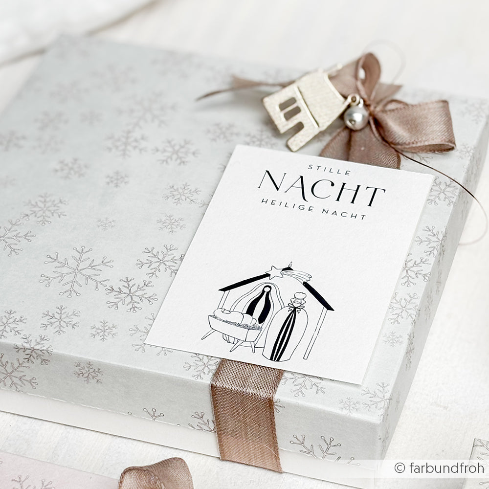 Als Geschenk verpackt in Alexandra Renke Schneeflocken Designpapier Weihnachtsmagie mit braunem Band, Ornament und einer Stille Nacht Krippenkarte - perfekt für Papierprojekte oder Buchbinderei Fans.